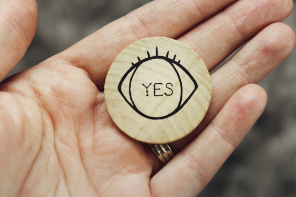 A person holding a wooden circle with an eye that says "yes."